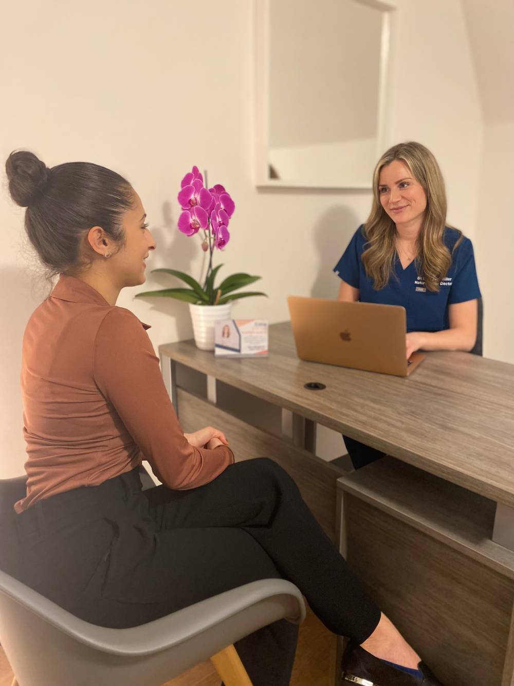 two women sitting at a table with a laptop